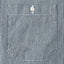 A closeup of the pocket of the hickory striped denim work shirt with a white button.