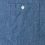 The front chest pocket of the light denim work shirt with a white button.