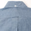 The back of the blue tuxedo shirt with a white button on the back of the collar and a locker loop.