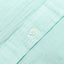 A white button on the stitched placket on the Teal Chambray Dobby Stripe shirt.