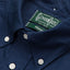 A navy-colored, button down 100% cotton Oxford shirt with an unlined collar, white buttons, green label, and stitching.